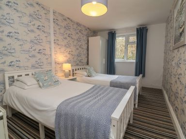 A bedroom with two single beds a nightstand with a lamp a wardrobe and striped carpet at Gatekeepers Cottage in Bilbrook near Minehead
