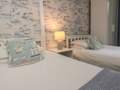 A bedroom with two single beds a nightstand with a lamp and nautical-themed wallpaper and cushions at Gatekeeper's Cottage in Bilbrook near Minehead