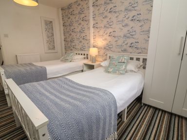 A bedroom with two single beds a nightstand with a lamp a mirror on the wall and a wardrobe at Gatekeeper's Cottage in Bilbrook near Minehead