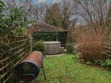 A garden with a rusty barbecue grill wooden hot tub and a shed covered in ivy at Gatekeeper's Cottage Bilbrook near Minehead