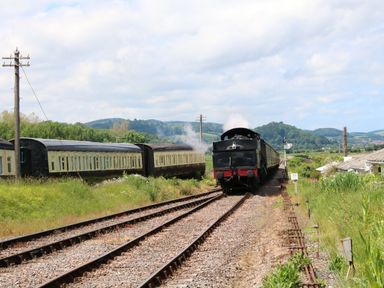 A steam locomotive pulling passenger cars on train tracks with green hills and signal posts in the background at Gatekeeper's Cottage in Bilbrook near Minehead