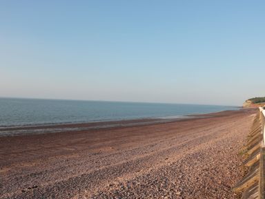 A pebble beach with calm sea and clear sky near a coastline with cliffs at Gatekeeper's Cottage in Bilbrook near Minehead