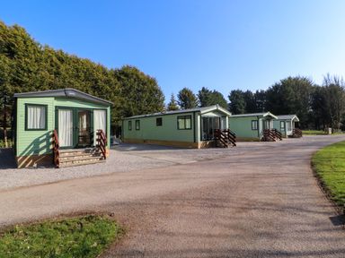 Four green mobile homes with steps on a gravel area near trees at Lodge 2 in Silverdale