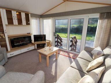 A living room with a sofa armchairs a coffee table TV and sliding glass doors at Lodge 2 in Silverdale