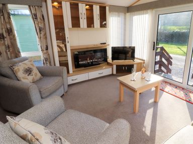A living room with two armchairs a coffee table a TV and sliding glass door at Lodge 2 in Silverdale