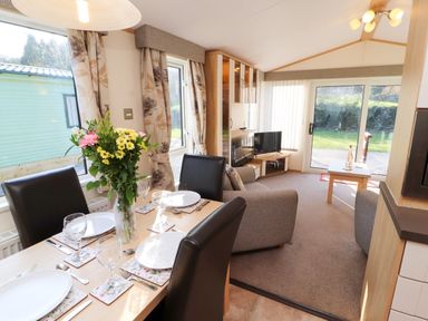 A dining table with plates and flowers next to a living room with chairs and a television at Lodge 2 in Silverdale