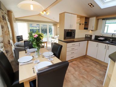 A dining table set with plates glasses and cutlery next to a kitchen with white cabinets and a microwave at Lodge 2 Silverdale