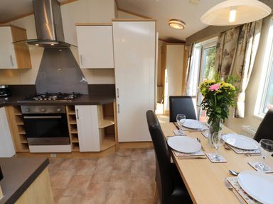 A kitchen with an oven stove and cabinets beside a dining table with plates glasses and a flower vase at Lodge 2 in Silverdale