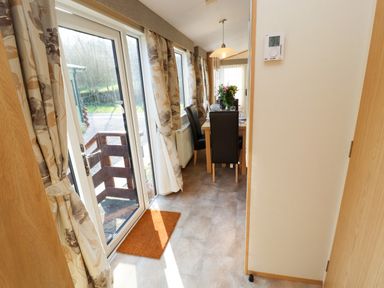 A dining area with a table set with plates and glasses and black chairs beside glass doors with floral curtains at Lodge 2 Silverdale