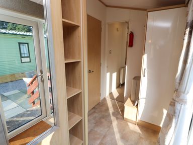 A hallway with wooden shelves a door a fire extinguisher and a window with patterned curtains at Lodge 2 in Silverdale