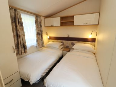 A bedroom with two single beds a window with floral curtains and overhead cabinets at Lodge 2 in Silverdale