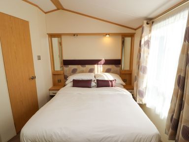 A bedroom with a bed pillows bedside tables mirrors a door and a window with curtains at Lodge 2 in Silverdale