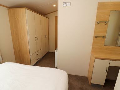 A bedroom with a bed a wardrobe and a dressing table with a mirror at Lodge 2 in Silverdale