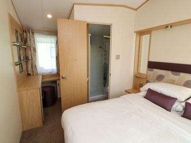 A bedroom with a bed pillows bedside tables a dressing table and an open door to a bathroom at Lodge 2 in Silverdale