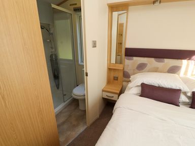 A bedroom with a bed and a bedside table next to an en suite bathroom with a shower and toilet at Lodge 2 in Silverdale