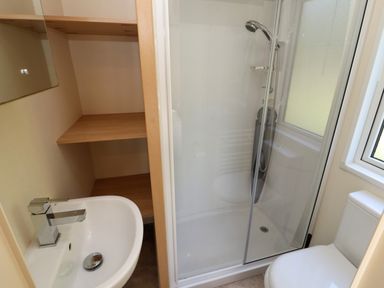 A bathroom with a sink a shower with glass doors wooden shelves a toilet and a window at Lodge 2 in Silverdale