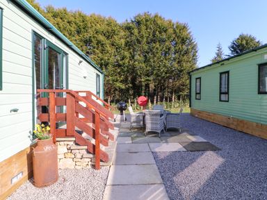 An outdoor area with two mobile homes a patio with table and chairs a barbecue and trees in the background at Lodge 2 in Silverdale