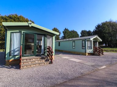 Two green mobile homes with steps in front on a gravel area with trees in the background at Lodge 3 in Silverdale