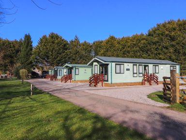 A row of green lodges with red railings next to a gravel driveway and green lawn at Lodge 3 in Silverdale