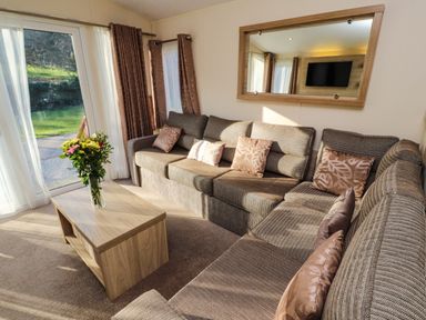 A living room with a brown sectional sofa a wooden coffee table with flowers and a large mirror on the wall at Lodge 3 in Silverdale