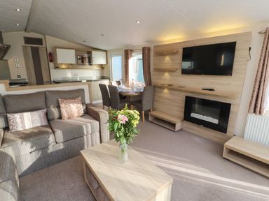 A living room with a sofa coffee table flowers dining table kitchen TV and fireplace at Lodge 3 in Silverdale