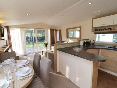 A dining table set with dishes and glasses next to a kitchen counter and a living area with sofa and sliding glass doors at Lodge 3 in Silverdale