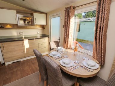 A dining area with a wooden table set for four and kitchen cabinets with a microwave at Lodge 3 in Silverdale