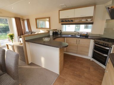 A kitchen with wooden cabinets a gas stove a countertop and a living area with chairs and a table with flowers at Lodge 3 in Silverdale