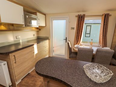A kitchen with wooden cabinets a dining table set with plates glasses and a bottle and a frosted glass door at Lodge 3 in Silverdale