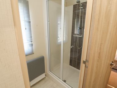 A bathroom with a shower enclosure a window with blinds a radiator with a towel and a wooden door at Lodge 3 in Silverdale