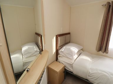 A small bedroom with a single bed pillows a bedside cabinet and a window with curtains at Lodge 3 in Silverdale