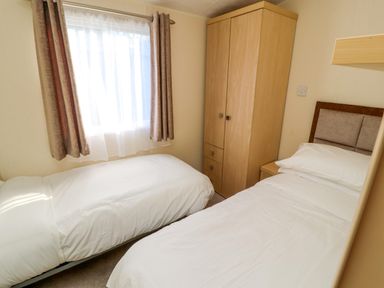 A bedroom with two single beds a wooden wardrobe and a window with curtains at Lodge 3 in Silverdale