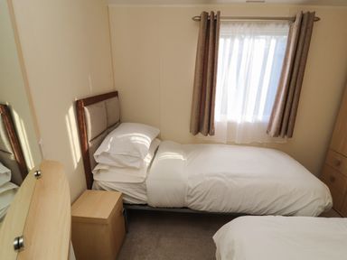 A bedroom with a single bed, bedside table, window with curtains, and part of another bed at Lodge 3 in Silverdale