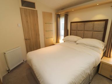A bedroom with a double bed a wooden door and windows with curtains at Lodge 3 in Silverdale