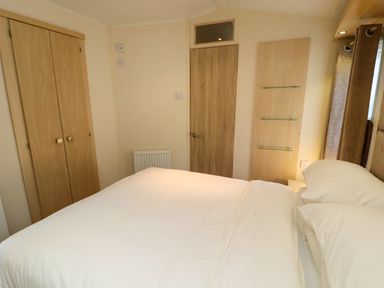 A bedroom with a double bed white bedding a wooden door a built in closet and glass shelves at Lodge 3 Silverdale