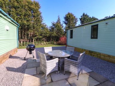 An outdoor patio area with a round glass table and four wicker chairs in between two light blue buildings at Lodge 3 in Silverdale
