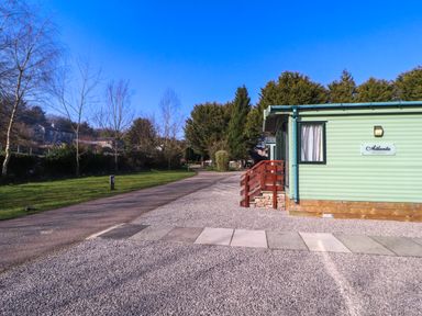 A green mobile home with a red wooden step next to a gravel path and trees in the background at Lodge 3 in Silverdale