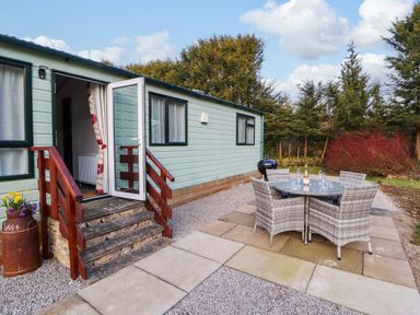 An outdoor patio with a round table and four chairs next to a small building with open door and steps at Lodge 4 in Silverdale