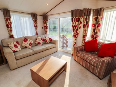 A living room with two sofas a wooden coffee table and floral curtains at Lodge 4 in Silverdale