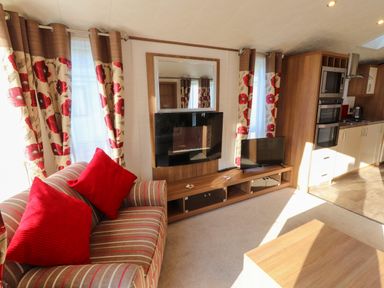 A living room with striped sofa and red pillows a television and floral curtains at Lodge 4 in Silverdale