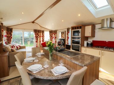 A kitchen and dining area with a marble countertop table set for four next to a living room with sofas and floral curtains at Lodge 4 in Silverdale
