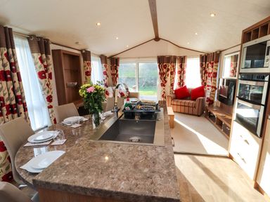 A kitchen island with a sink and dining set next to a living area with sofas and red floral curtains at Lodge 4 in Silverdale