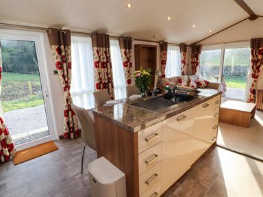 A kitchen island with a sink and chairs in a living area with patterned curtains and a sofa at Lodge 4 in Silverdale