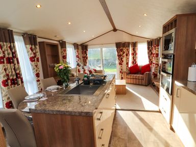 An open plan kitchen and living area with a dining table set for four and a sofa with red cushions at Lodge 4 in Silverdale