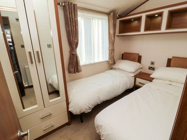 A bedroom with two single beds a nightstand a wardrobe with mirrors and a window with curtains at Lodge 4 in Silverdale