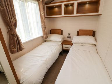 A bedroom with two single beds separated by a nightstand under wall shelves at Lodge 4 in Silverdale