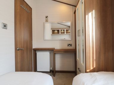 A bedroom with two single beds a wooden door mirror wardrobe and a radiator at Lodge 4 in Silverdale