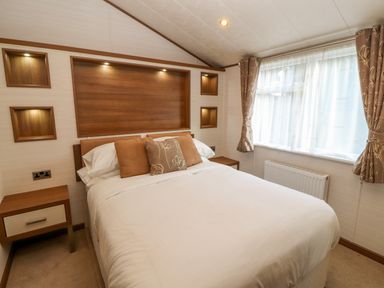 A bedroom with a double bed two bedside tables and a window with curtains at Lodge 4 in Silverdale