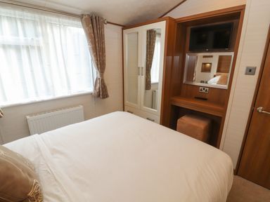 A bedroom with a bed wardrobe a mirror TV and curtains at Lodge 4 in Silverdale