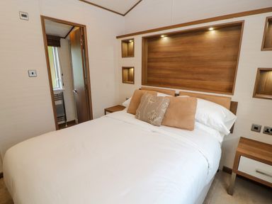 A bedroom with a double bed white bedding brown cushions wooden headboard and bedside tables at Lodge 4 in Silverdale